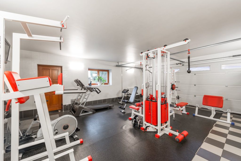 Home gym with exercise equipment and machines in a bright, spacious room with rubber flooring and white walls
