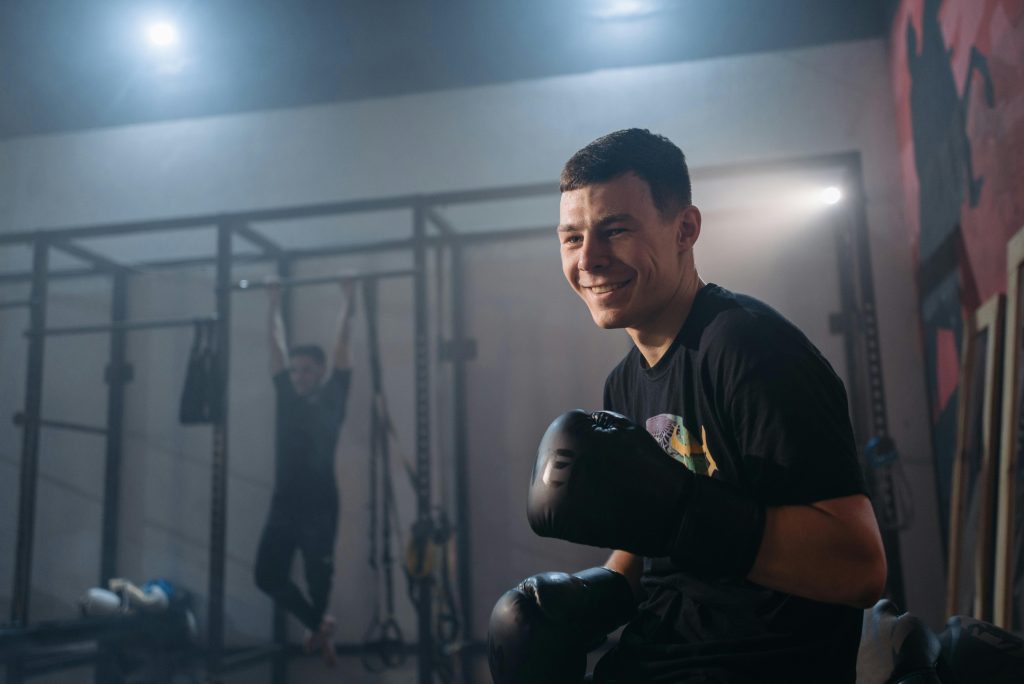 A young male boxer smiling during a training session inside a gym.